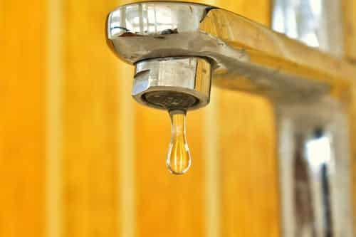 Inspire fresh plumbing blog ideas with a close-up of a chrome faucet, featuring a single water drop against a soft yellow backdrop.